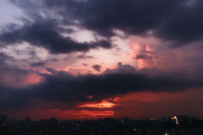 Silhouette city against dramatic sky during sunset