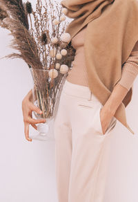 Midsection of woman holding plant in glass vase with hands in pocket