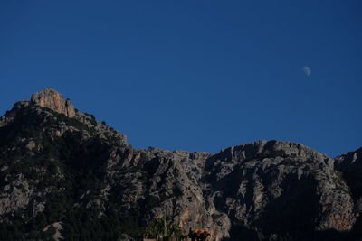 Low angle view of rocks against clear blue sky