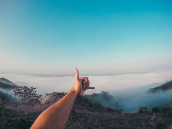 Cropped hand showing shaka sign against sky