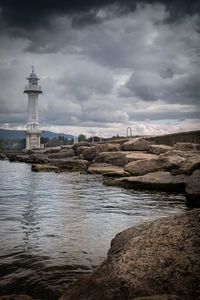 Lighthouse by sea and buildings against sky