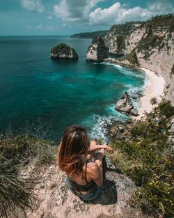 High angle view of woman sitting on rock by sea