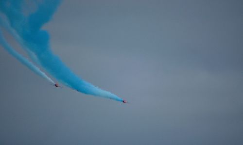 Red arrows jets sweep across sky with blue vapor trailing behind