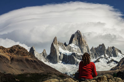 Rear view of woman sitting on rock against cloudy sky