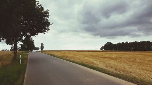 Road by agricultural field against sky