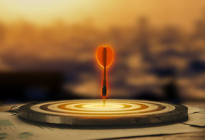 Close-up of lit candle against orange sunset sky