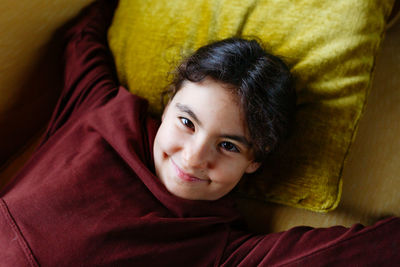 Close up portrait of smiling girl with dark hair lying on yellow sofa