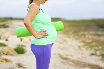 Midsection of pregnant woman with exercise mat standing on land