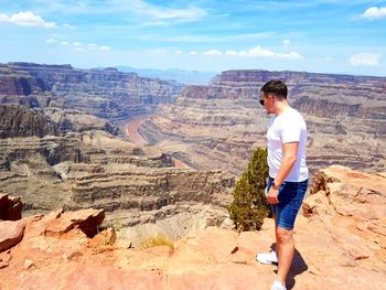 Rear view of man standing on rock against sky