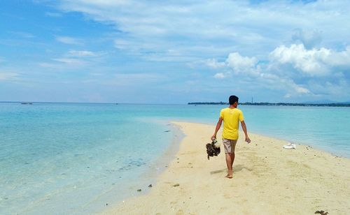 Rear view of man with seaweed walking at beach