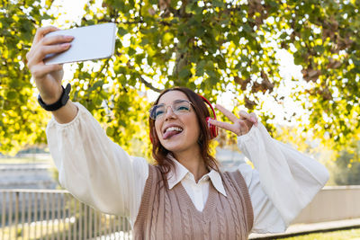 Businesswoman with glasses showing tongue out and having fun while making selfie and listening music