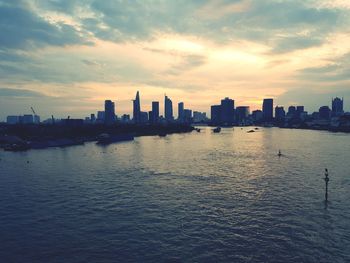 Sea by buildings against sky during sunset