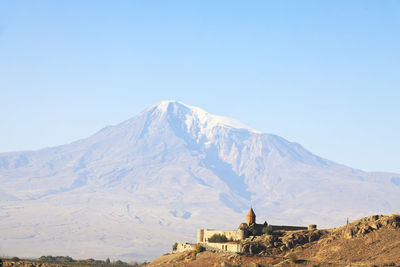 Scenic view of built structure against snowcapped mountain and sky