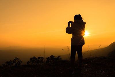 Silhouette woman photographing at sunset