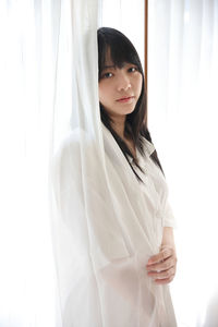 Portrait of young woman standing against curtain
