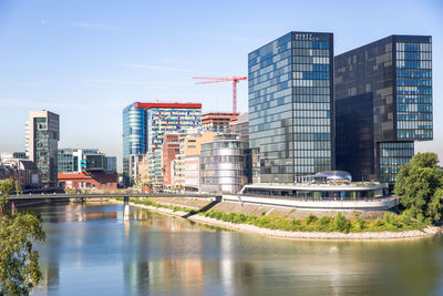 Modern buildings by river against sky in city