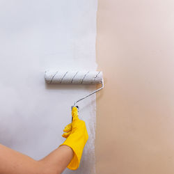 Girl child in yellow gloves paints a wall with a roller with white paint