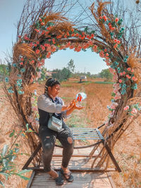 Full length of man photographing while sitting on tree