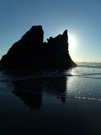Silhouette rock formations by sea against clear sky