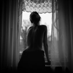 Rear view of woman looking through window at home