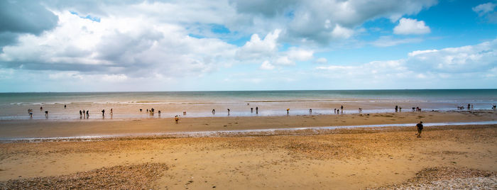 Panoramic view of beach against sky. people digging clams