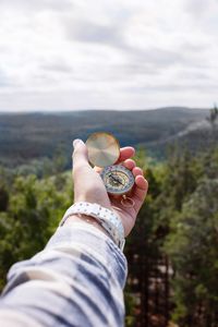 Cropped hand holding navigational compass against sky