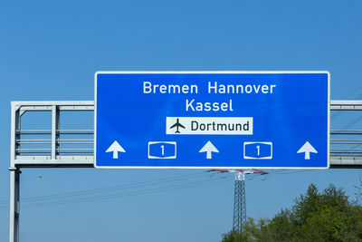 Low angle view of road sign against clear blue sky