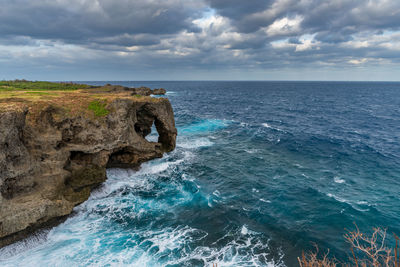 Scenic view of sea by cliff against cloudy sky