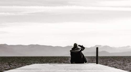 Rear view of woman sitting on mountain against sky