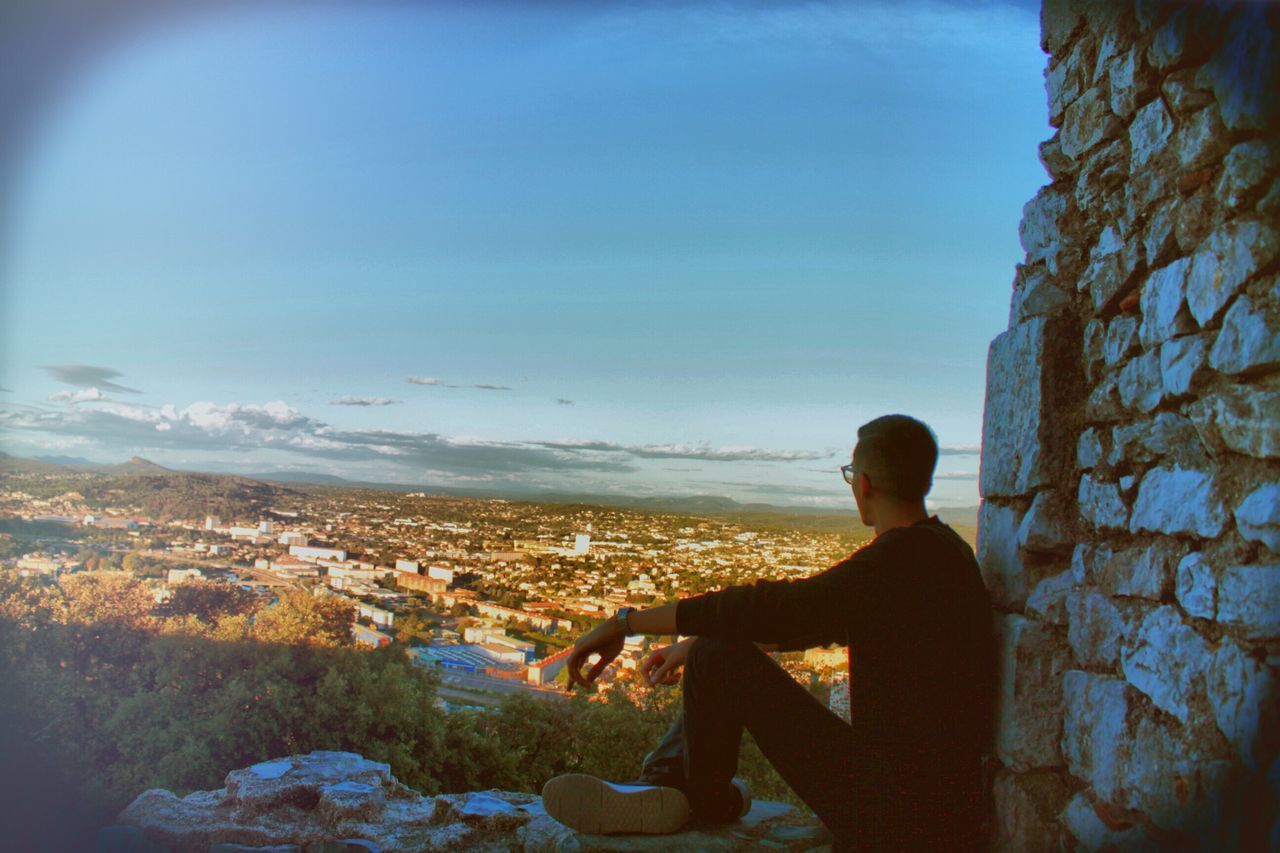 YOUNG MAN LOOKING AT CITYSCAPE AGAINST SKY