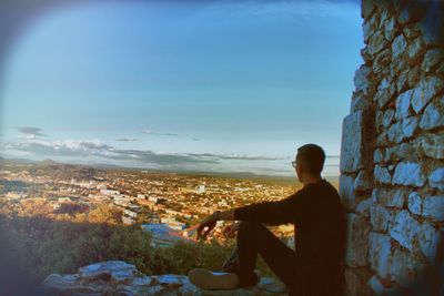 Man sitting on looking at cityscape against sky