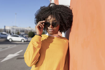 Young woman wearing sunglasses leaning on wall