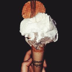 Close-up of hand holding ice cream against black background