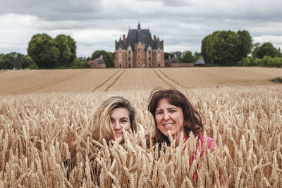 Two women travelers in a field of wheat ears in front of a renaissance castle.