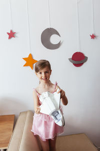 Portrait of smiling girl holding toy against wall at home