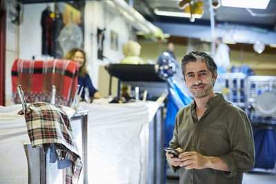 Portrait of smiling mature male worker standing with mobile phone in workshop