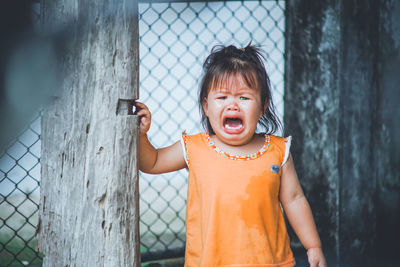Portrait of girl crying while standing against fence