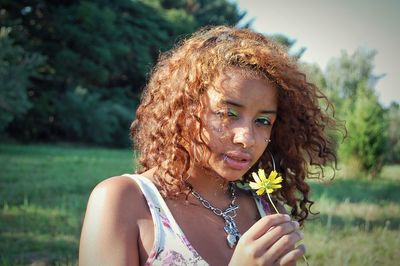 Portrait of beautiful woman holding flower and standing on field