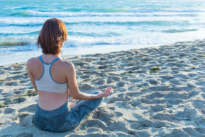 Rear view of young woman doing yoga on shore at beach