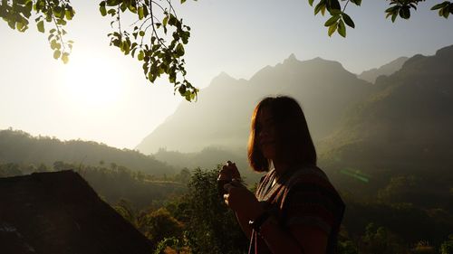 Portrait of woman holding coffee cup by mountains against sky