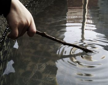 Cropped hand of person dipping stick in water
