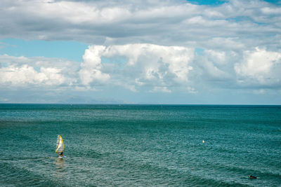 Scenic view of windsurfer and surfer in sea against sky