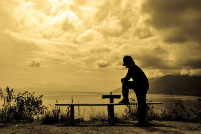 Side view of silhouette man sitting against sky during sunset