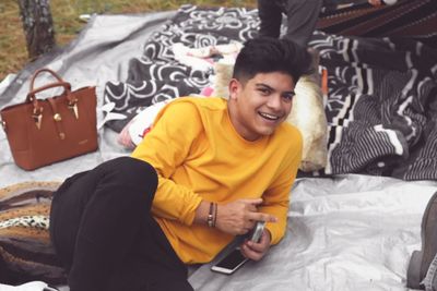 Portrait of smiling young man using mobile phone while sitting on bed