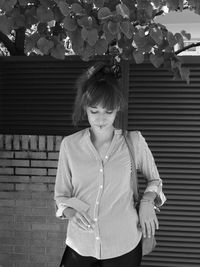 Woman holding cigarette while standing against fence wall