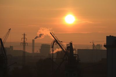 Silhouette cranes at construction site against sky during sunset