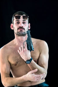 Shirtless man attempting suicide with gun against black background