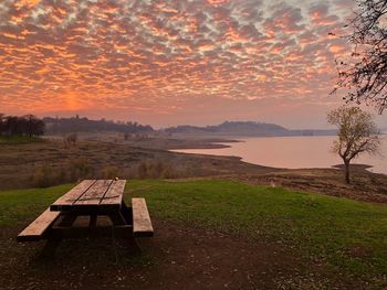 Empty bench on field against sky during sunset