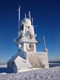 Low angle view of snow covered communication tower against clear blue sky