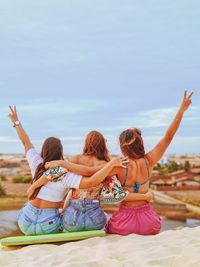 Rear view of cheerful female friends sitting on sand